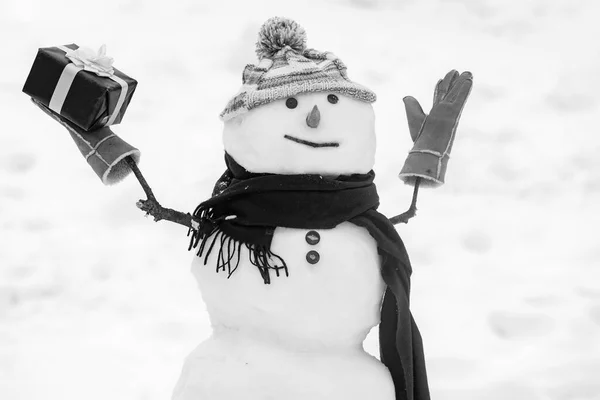 Cute snowman in hat and scarf on snowy field with surprise Christmas gift. Snowman with shopping bag - gift shopping concept. Happy smiling snow man - sale discount concept. — Stock Photo, Image