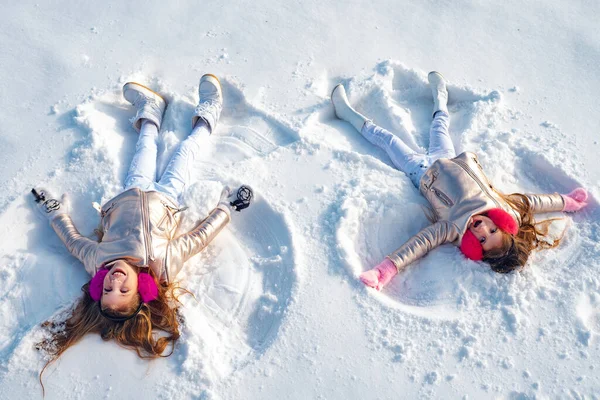 Två små flickor som gör snö ängel medan de ligger på snö. Lycklig flicka på en snö ängel visar. — Stockfoto