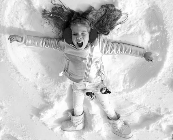 Tjejen på en snöängelshow. Leende barn liggande på snö med kopieringsutrymme. En lustig grabb som gör snöängel. Ovanifrån. — Stockfoto