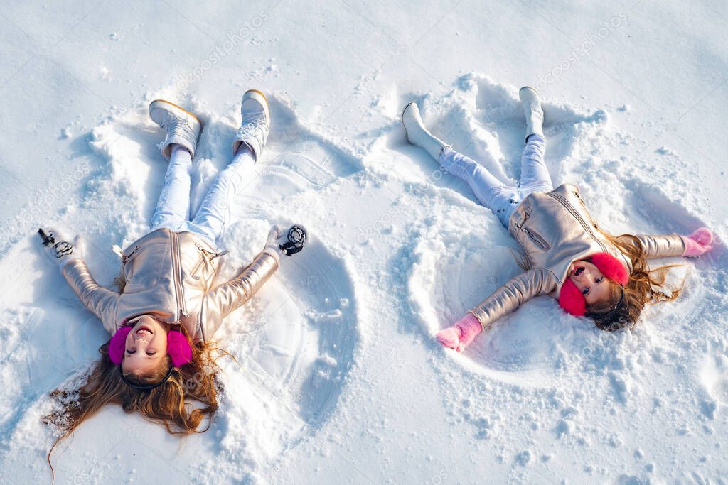 Two little girl making snow angel while lying on snow. Happy girl on a snow angel shows.