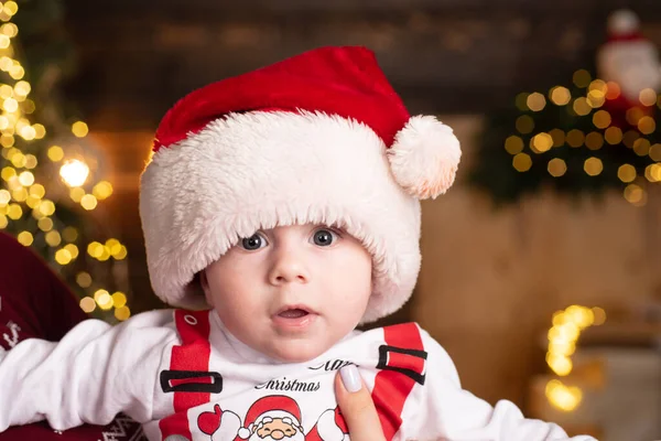Cute baby face w Santa kapelusz w pobliżu choinki. Wesołego dzieciństwa, wesoły dzieciaku. Noworoczne dzieci. — Zdjęcie stockowe