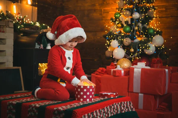 Criança feliz com caixa de presente de Natal. Decoração de Natal. Criança feliz abrindo caixa de presente de Natal. Bebê engraçado vestido com chapéu de Papai Noel. Luz LED. — Fotografia de Stock