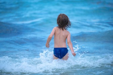 Denizde oynayan mutlu çocuk. Arka planında beyaz büyük dalgalar olan mavi okyanus..