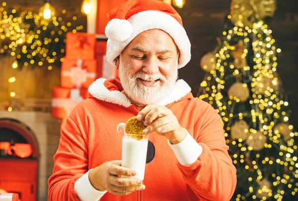 Santa drží sušenku a sklenici mléka na vánoční stromeček pozadí. Santa Claus drží vánoční cukroví a mléko na pozadí vánoční strom. — Stock fotografie