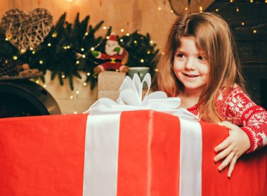 Gülümseyen mutlu küçük kız elinde Noel Baba 'dan dev bir hediye tutuyor. Noel arifesi ve sihirli konsept. Parlak bir yeni yıl arifesi. Hediye verme ve alma kavramı.