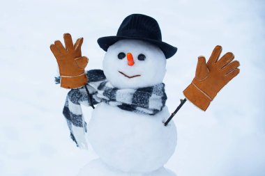 Kar taneleri ve kardan adamla kışın. Kardan adam kırmızı burunlu, kış şapkası ve eşarbıyla duruyor..