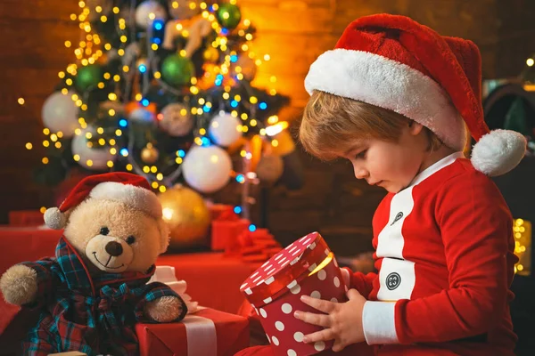 Criança menino feliz com presente ou caixa de presente dentro de casa. Criança com um presente de Natal no fundo da casa de madeira. — Fotografia de Stock