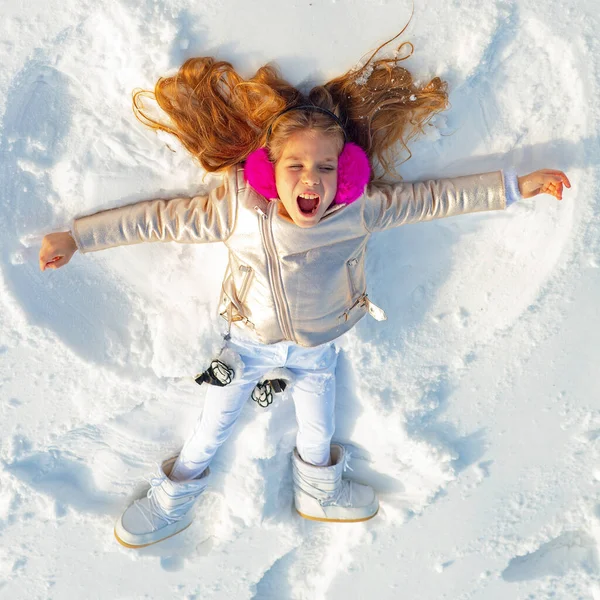 Tjejen på en snöängelshow. Leende barn liggande på snö med kopieringsutrymme. En lustig grabb som gör snöängel. Ovanifrån. — Stockfoto