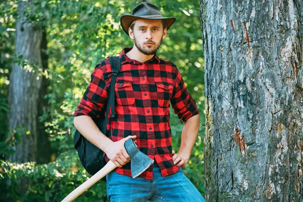 一个拿斧头的英俊男人时髦的年轻人摆出一副木匠的架势.森林砍伐是土地退化和破坏自然生态系统稳定的一个主要原因. — 图库照片