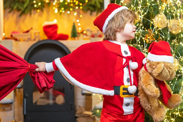 Férias em família. Menino criança jogar perto da árvore de Natal. Desejo conhecer o Pai Natal. Papai Noel ajudante carregando grande saco cheio de presentes. Acredite no milagre de Natal. — Fotografia de Stock