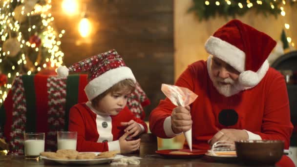 Dziadek i wnuk gotują ciasto w kuchni w Boże Narodzenie. Przygotuj Boże Narodzenie i Nowy Rok. Szczęśliwy Mikołaj z dzieckiem w kapeluszu wakacje. — Wideo stockowe