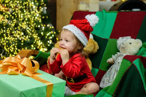 Nettes Babygesicht mit Weihnachtsmütze in der Nähe des Weihnachtsbaums. Glückliche Kindheit, Kind 1 Jahr alt. Neujahrskinder. Weihnachtswunder, magische Geschenkbox und ein kleines Mädchen. — Stockfoto