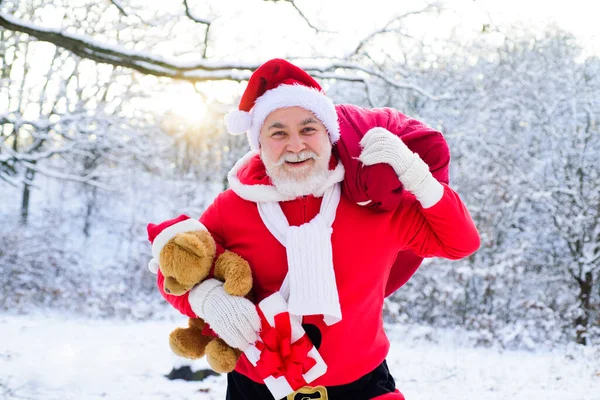 サンタはクリスマスプレゼント、雪の風景の袋で冬の森に歩いてください。明けましておめでとうございます. — ストック写真