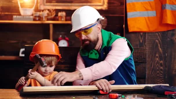 Hijo experto en delantal usando martillo mientras trabaja en muebles de madera con padre en carpintería. Feliz paternidad.. — Vídeo de stock