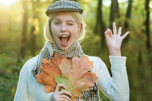 Femme d'automne. Joyeux clin d'oeil automne fille. Joyeux insouciante femme d'automne dans le parc par une journée ensoleillée. Fille jouer avec des feuilles sur fond de feuilles d'automne. — Photo