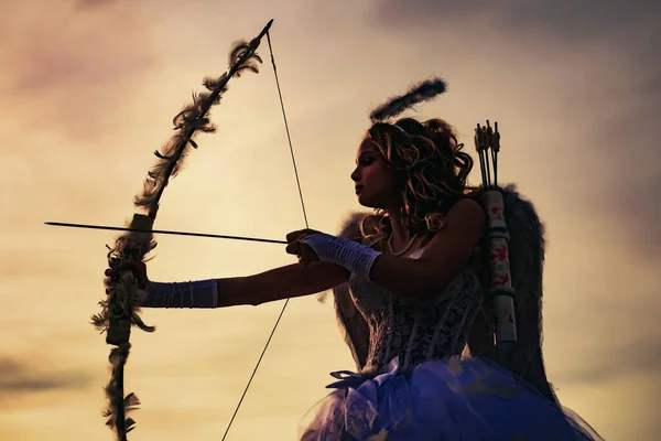 Silueta de un cupido. Vista lateral del arquero adolescente contra el atardecer. Niña Cupido apuntando a alguien con una flecha de amor. — Foto de Stock