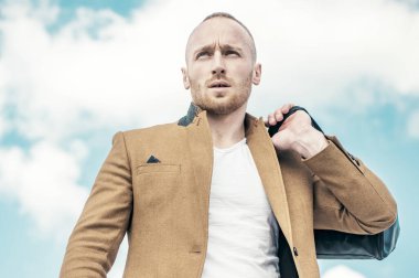 Takım elbiseli, güneş gözlüklü ve bulutlu gökyüzüne bakarken yüzünü çeviren yakışıklı genç adamın yakın çekimi. Bayım. Mükemmellik. Adam bulunmaya hazır. Yeni bir hayatın beklentisiyle.