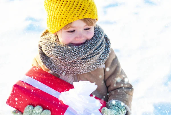 雪の中のクリスマスの子供たち。冬休みのコンセプト。素敵な休日をお過ごしください。お正月と陽気なクリスマス。幸せな冬の子供は贈り物弓雪の背景を保持します。冬服のかわいい男の子の帽子 — ストック写真
