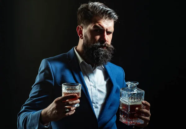 Barman skórzany fartuch trzymający koktajl whisky w szkle. Hipster z brodą i wąsami w garniturze pije alkohol po dniu pracy. — Zdjęcie stockowe