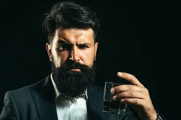 Luxus-Alkoholgetränk. Degustation von Elitealkohol. Selbstbewusster bärtiger Mann im schwarzen Anzug mit Glas Whisky auf dem Dachboden. — Stockfoto