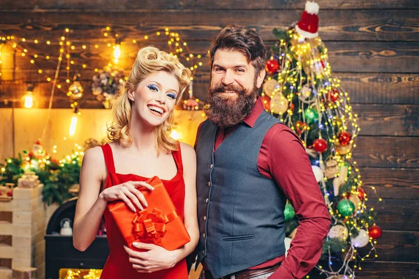 Sexy couple with gift over Christmas tree background. Portrait of a beautiful couple in Christmas dress holding gift while standing and looking up over Christmas tree background. — Stock Photo, Image