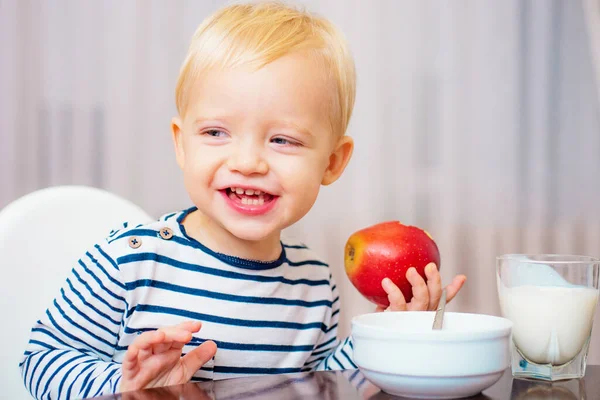 Een leuke jongen zit aan tafel met bord en eten. Gezond eten. Een leuke baby die ontbijt eet. Babyvoeding. Eet gezond. Peuter neemt een snack. Gezonde voeding. Vitamine concept. Kind eet appel — Stockfoto