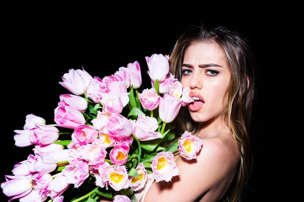 一个带着花的年轻女人美丽的姑娘把一束郁金香束在黑色的背景上，带着性感的表情粘在舌头上. — 图库照片