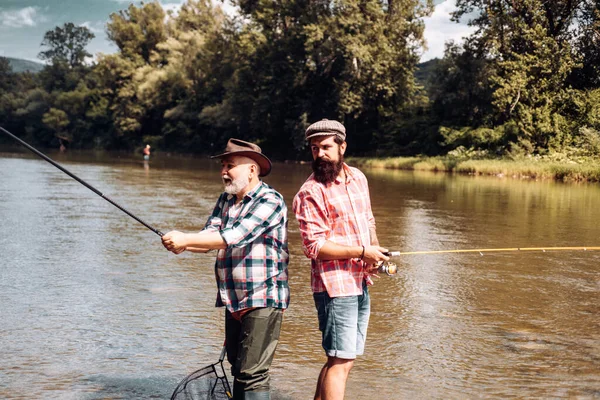 Two fishermen relaxing together while fishing on the lake at the morning. Fly fishing adventures. Family day. If wishes were fishes. Man at riverside enjoy peaceful idyllic landscape while fishing. — Stock Photo, Image