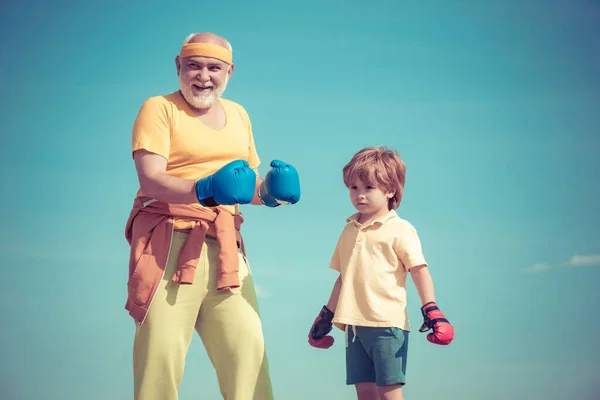 Retrato de un determinado boxeador senior con niño pequeño sobre fondo azul del cielo. Boxeador abuelo y niño con guante de boxeo azul sobre fondo de cielo azul - aislado. — Foto de Stock