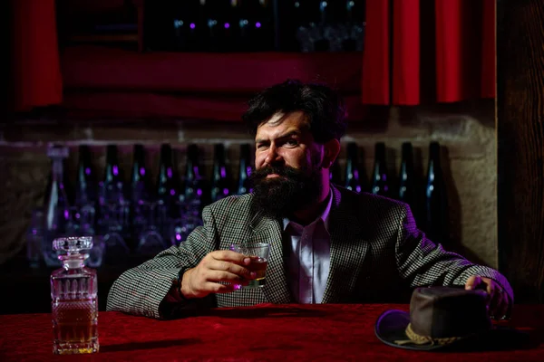 Bonito homem pensativo está segurando um copo de uísque e olhando para longe enquanto sentado no bar dentro de casa. — Fotografia de Stock