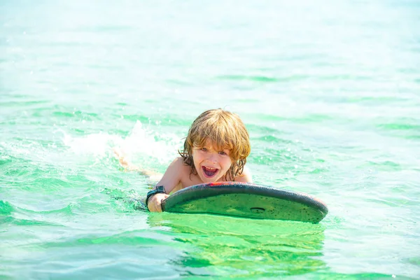 Niño nadando con tabla de surf en la playa en el mar azul en verano. Océano azul con wawes. Niño nadando en el mar. — Foto de Stock