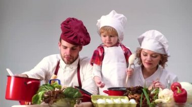 Şef şapkasıyla yemek yapan genç bir aile. Çiftler ve çocuklar evde birlikte yemek yaparken eğleniyor, mutlu gülümseyen ebeveynler hafta sonunun keyfini çıkarıyor küçük çocuklarla mutfakta fırın pişiriyorlar..