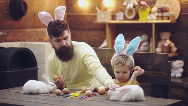 Батько і син у великодніх вухах кролика. Смішні обличчя. Щаслива сім'я малює яйця. Білий кролик символ Великодня . — стокове відео