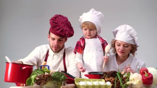 シェフの帽子で若い家族料理。カップルと子供は一緒に家で楽しい料理のベーキングを持っています、幸せな笑顔の両親は台所でパン屋料理をしている小さな子供たちと週末の遊びを楽しむ. — ストック動画