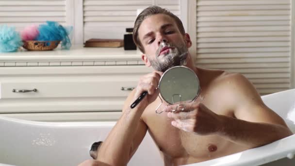 Młody człowiek golił twarz przy lustrze w łazience. Mężczyzna piękno, pielęgnacja brody koncepcji pielęgnacji skóry. — Wideo stockowe