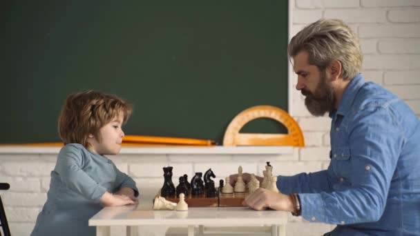 Pai e filho a jogar xadrez. Um rapazinho esperto a pensar em xadrez. Jogos e atividades para crianças. Pai e criança relaxando juntos. — Vídeo de Stock