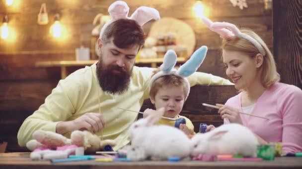 Joyeux Pâques. Préparer la famille pour Pâques. Les parents avec enfant peignent des œufs de Pâques. Mère, père et fils portant des oreilles de lapin. Visages souriants. — Video