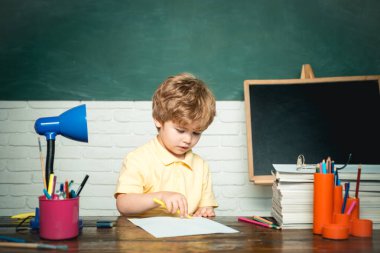 Okulda tahtaya yakın bir çocuk. Küçük komik çocuklar tahtayı işaret ediyor. Çalışmaya biraz hazır. Karatahta masasının yanındaki sınıfta tatlı bir çocuk. Eğitim.