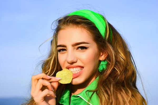 Uśmiechnięta kobieta je chipsy. Młoda kobieta gryzie kawałek chipsów ziemniaczanych zębami. Smaczne pyszne fast food. Jem chipsy. Słodka kobieta je niezdrową przekąskę. Fast food sexy kobieta model. — Zdjęcie stockowe