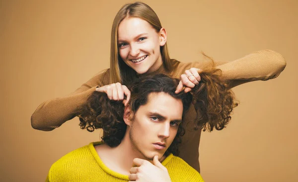 一对年轻夫妇在开一个关于孤立的卡其布背景的玩笑一个金发碧眼的女朋友给她卷发的男朋友留着滑稽的发型. — 图库照片