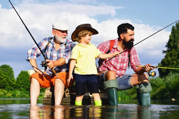 Un uomo che insegna ai bambini a pescare nel fiume. Nonno, padre e ragazzo pescano insieme. Papà e figlio pesca al lago. Weekend estivo. — Foto Stock