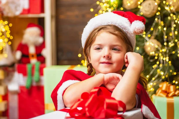 Malá Santa Claus dívka dárek. Vtipný kluk držící vánoční dárek. Roztomilé dítě u vánočního stromečku. Zimní vánoční emoce. — Stock fotografie