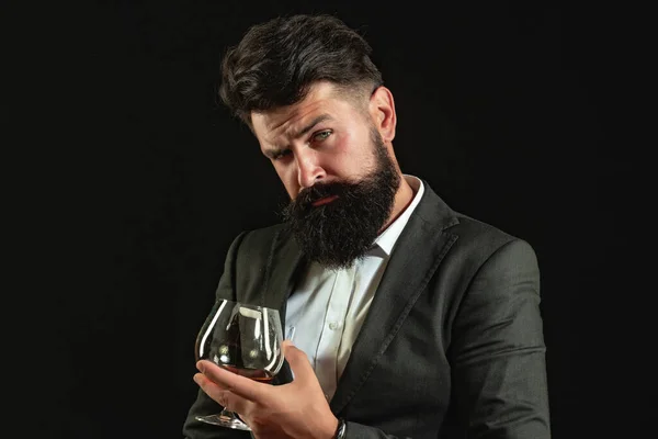 Przystojny brodaty biznesmen pije drogą whisky. Sommelier człowiek. Człowiek z brodą trzyma szklankę brandy. — Zdjęcie stockowe