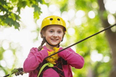 Küçük mutlu çocuk halatla oyun sahasına tırmanıyor. Ağaç evde ya da halat parkında güvenlik ekipmanlarına tırmanan sevimli bir çocuk ipe tırmanıyor. Yürümeye başlayan anaokulu.