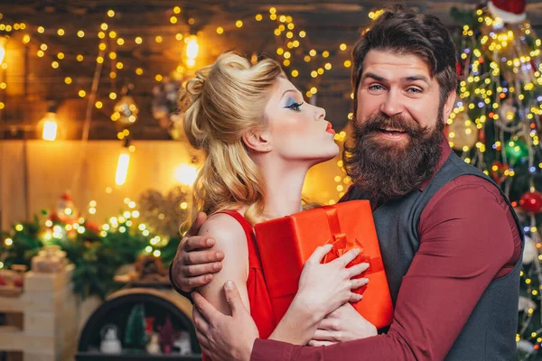 Glad jul par kyssas och kram med röd presentförpackning över hem julgran bakgrund. Förvånade par. Glada par fira semester. — Stockfoto