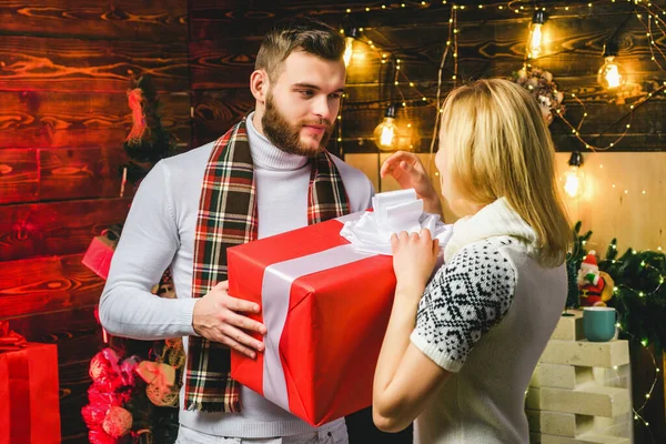 Unga par kär sitter bredvid en fint dekorerad julgran utbyta julklappar. Romantiskt par utbyter julklappar hemma. Nyårsafton. — Stockfoto