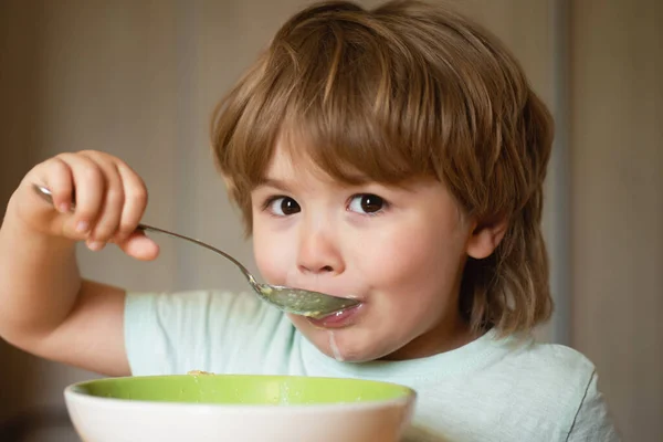 Schattig kind dat thuis ontbijt eet. Ouderschap. Baby eten. Jong kind zit op de tafel te eten met een grappige uitdrukking op zijn gezicht. Lachende vrolijke schattige baby eten fruit puree in de keuken. — Stockfoto