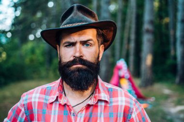 Tişörtlü, şapkalı, sakallı, olgun bir adam. Sakallı adam ormanda rahatlar. Ciddi sakallı adam. Ormanda çekici bir turist. Saç sakalı bakımı. Yaz kampı. Uzun sakallı vahşi bir kovboy. Saç sakalı bakımı.