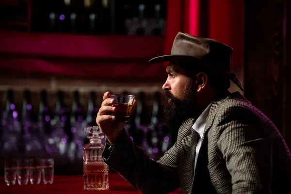 Atrakcyjny brodaty mężczyzna w barze z whiskey. Hipster z brodą i wąsami w garniturze pije alkohol po dniu pracy. — Zdjęcie stockowe