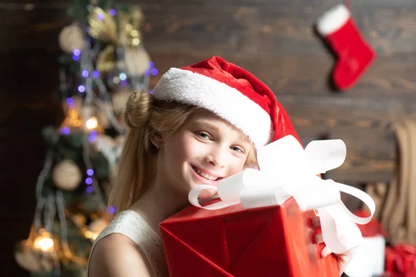 Ráno před Vánocemi. Portrét dítě s dárkem na dřevěném pozadí. Roztomilé holčička zdobí vánoční stromeček uvnitř. — Stock fotografie